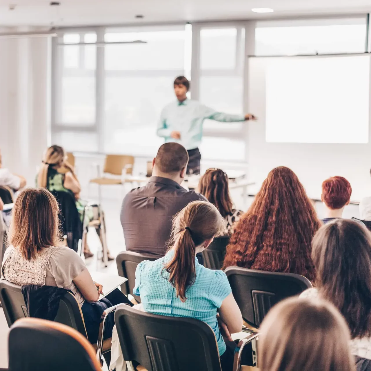 Business and entrepreneurship symposium. Speaker giving a talk at business meeting. Audience in conference hall. Rear view of unrecognized participant in audience.